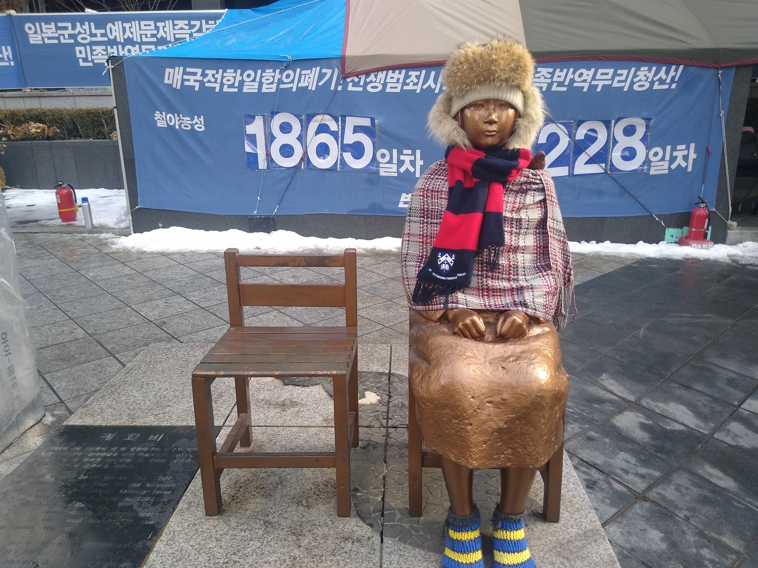The Statue of Peace in front of the former Japanese Embassy in Seoul, South Korea commemorates comfort women, sex slaves taken by the Imperial Japanese Army during World War II. The slogans on the tarp behind the statue demand the Japanese government to make reparations.